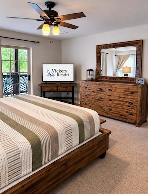 Une chambre à coucher comprenant un lit, une commode, un ventilateur de plafond, un téléviseur et une porte donnant sur un balcon.