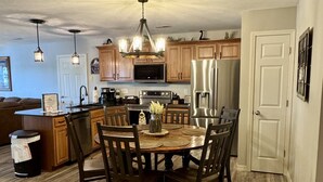 A modern kitchen with wooden cabinets, a central island, and a dining area with a round table and chairs.