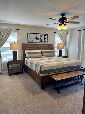 A bedroom with a wooden bed, two bedside tables, a ceiling fan, and a wall-mounted sign.