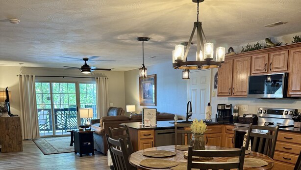 A spacious living area with a dining table, wooden chairs, a ceiling fan, and a kitchen area with modern appliances.