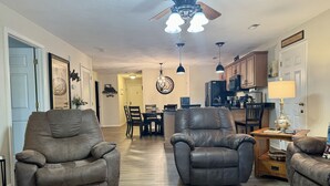 A spacious living room with two leather armchairs, a dining area with a wooden table and chairs, a kitchen with wooden cabinets, and a ceiling fan. - Lakefront Condo A-2 at Vickery Resort by RedAwning (Hollister)