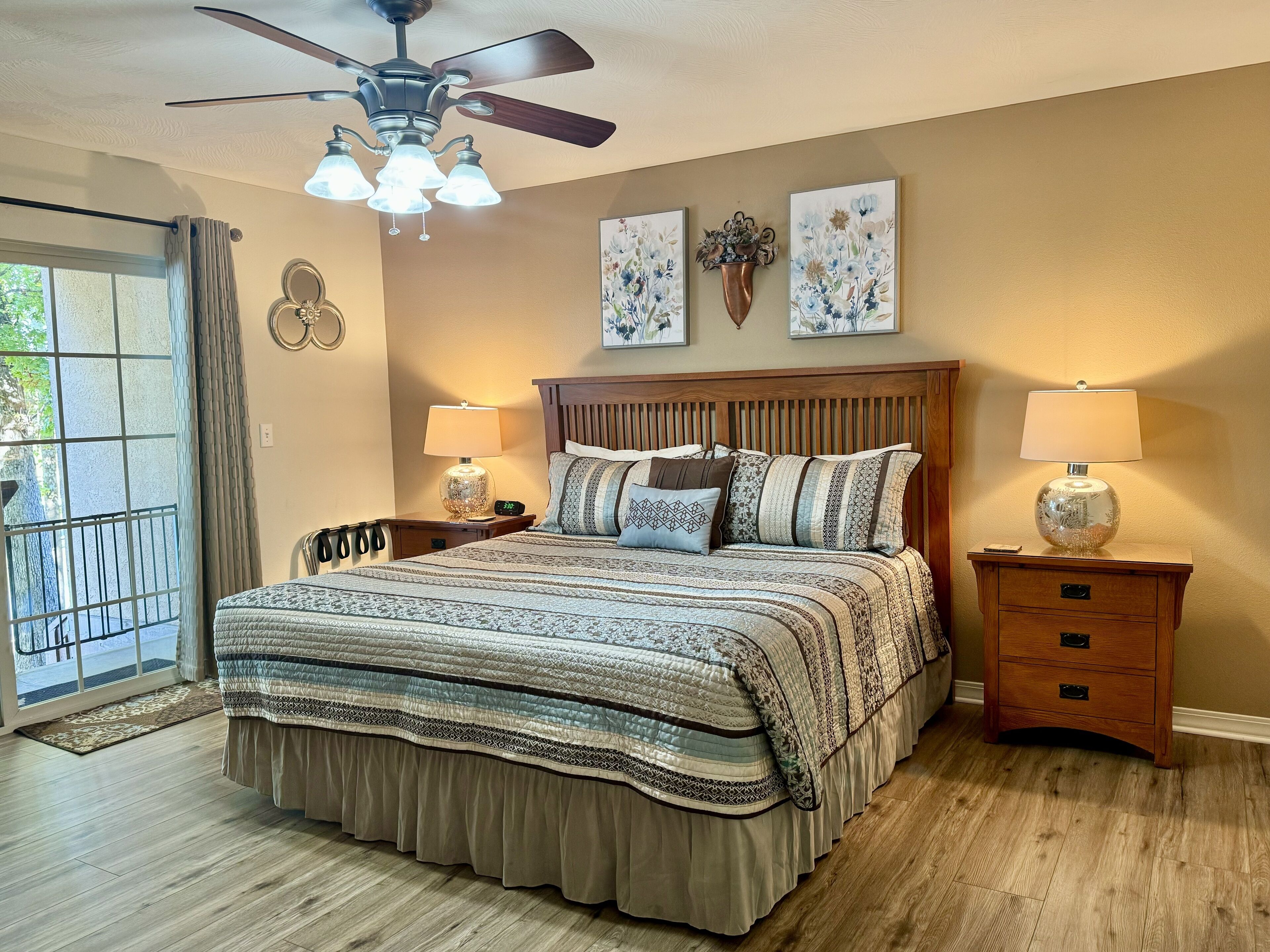 A bedroom with a bed, two bedside tables with lamps, a ceiling fan, and artwork on the wall.