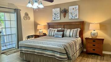 A bedroom with a bed, two bedside tables with lamps, a ceiling fan, and artwork on the wall.