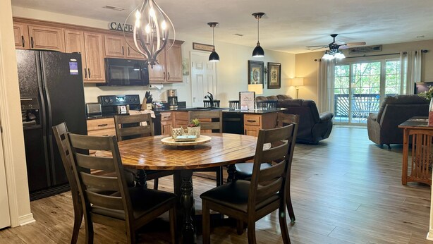 A spacious kitchen with wooden cabinets, a dining table with chairs, and a living area with a couch and a TV. - Lakefront Condo A-2 at Vickery Resort by RedAwning (Hollister)