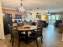 Una cocina amplia con armarios de madera, una mesa de comedor con sillas y una sala de estar con sofá y televisor.