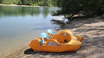 A small inflatable boat on a gravel shore near a lake.