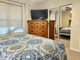 A bedroom with a bed, a dresser, a television, and a mirror.