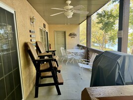 Un patio cubierto con mobiliario exterior, incluyendo sillas de madera y una mesa, y un ventilador de techo.