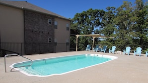 Une piscine rectangulaire avec un escalier en métal, entourée d’une terrasse en béton. Plusieurs chaises Adirondack bleu clair sont disposées autour de la piscine.