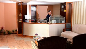 A reception area with a counter, a sofa, and a wicker chair. - Hotel Imperial (Mossoro)