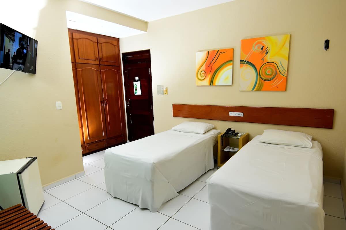 Habitación de hotel con dos camas individuales, un armario de madera, un televisor y una decoración abstracta en la pared.