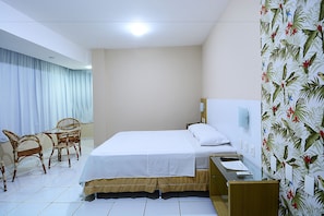 Quarto de hotel com cama, escrivaninha, cadeira e cortina.