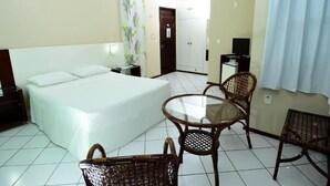 A hotel room with a bed, a glass-top table, wicker chairs, a TV, and a door leading to another room. - Hotel Imperial (Mossoro)