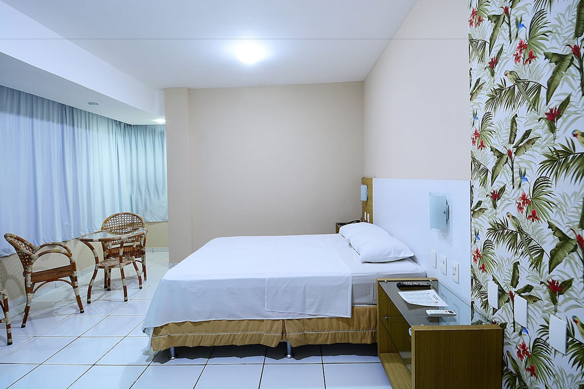 Una habitación de hotel con cama, escritorio, silla y ventana con cortinas.