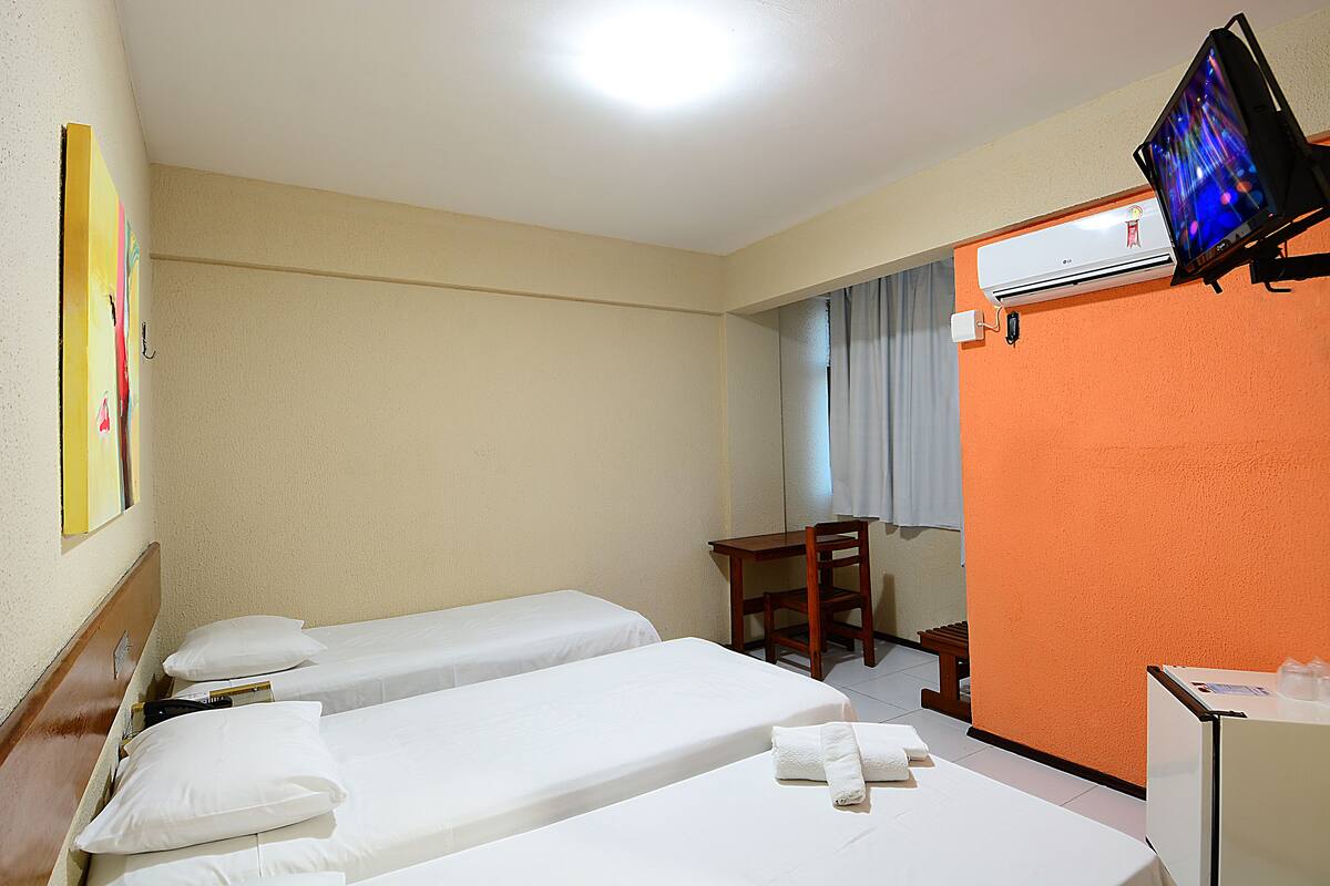 Una habitación de hotel con dos camas individuales, un escritorio, una silla, un televisor y un equipo de aire acondicionado.