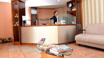 A reception area with a counter, a glass display table with magazines, a beige sofa, and a clock on the wall.