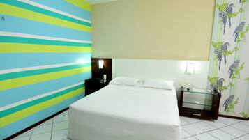A hotel room with a bed, a nightstand, a glass cabinet, and a wall with a striped pattern.
