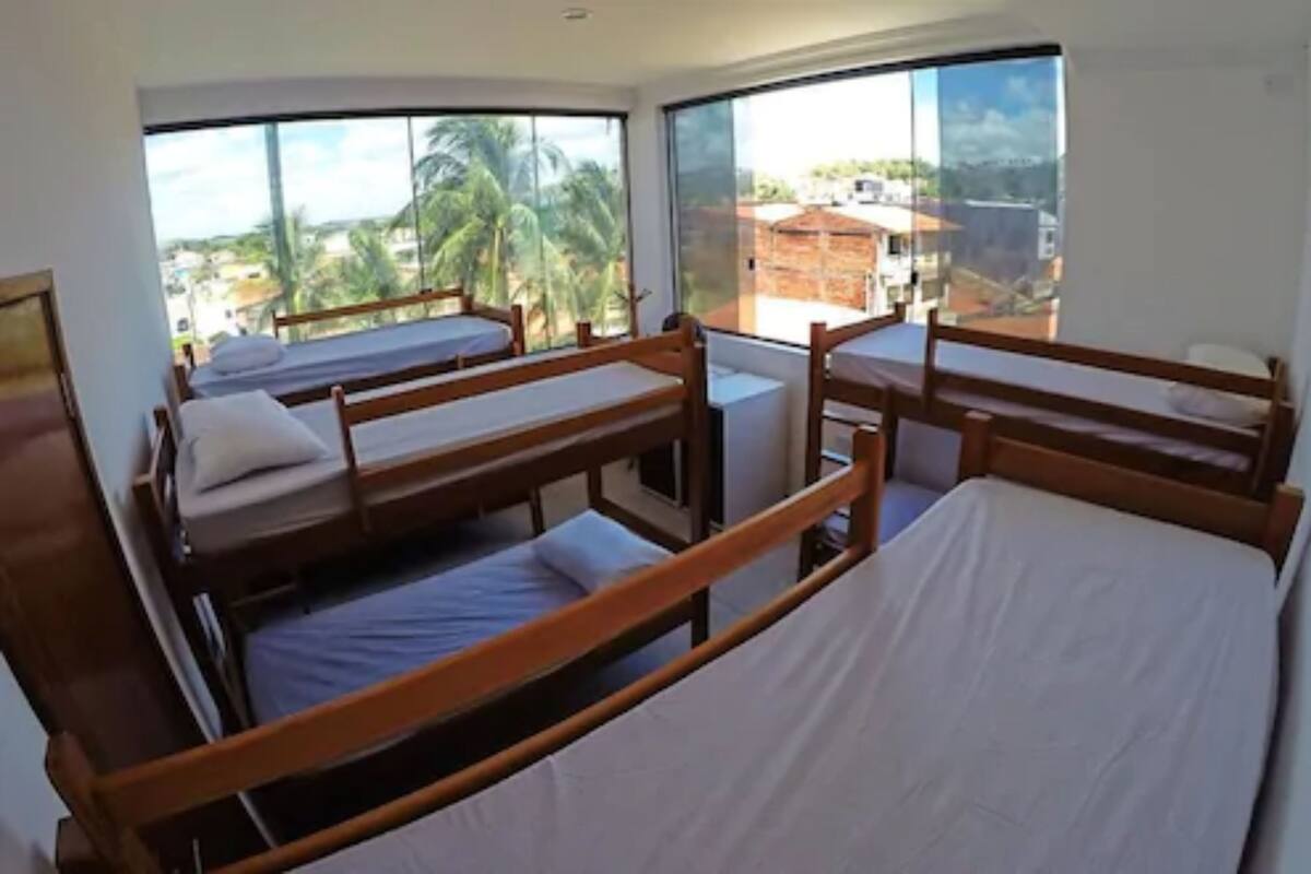 Una habitación con literas, ventanas amplias y vistas a palmeras y edificios.