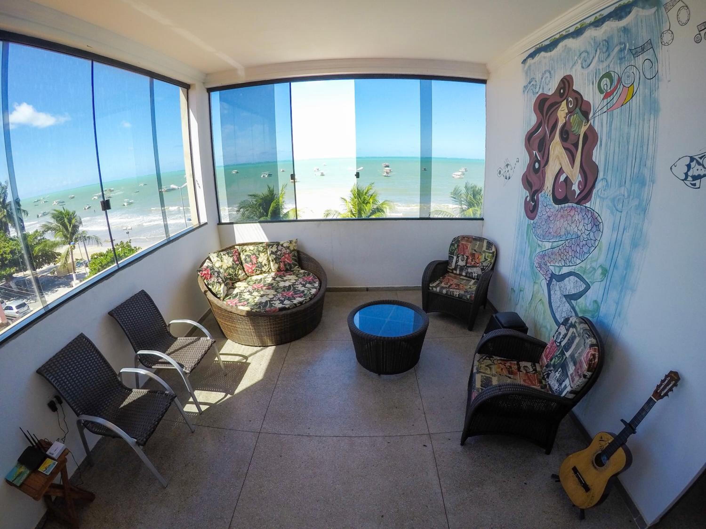 A balcony with a view of the ocean, wicker furniture, a guitar, and a mural.