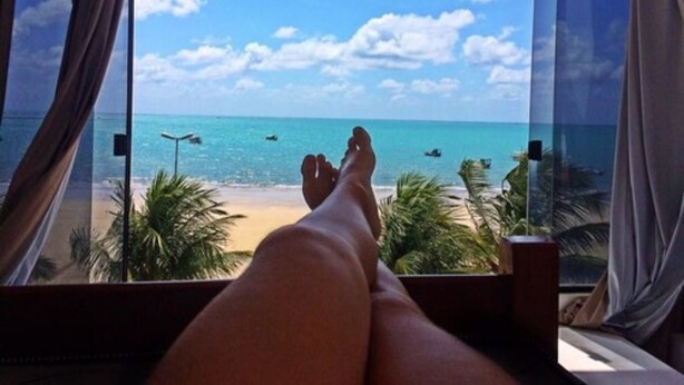 A view of a beach from a window with curtains, featuring a clear sky and calm sea. - Maraga Beach Hostel (Maragogi)