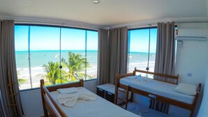 A room with two bunk beds, a small table, and a window with a beach view. - Maraga Beach Hostel (Maragogi)