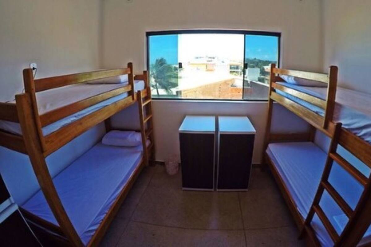 Una habitación con dos camas literas de madera, una mesita pequeña y una ventana con vistas a edificios.