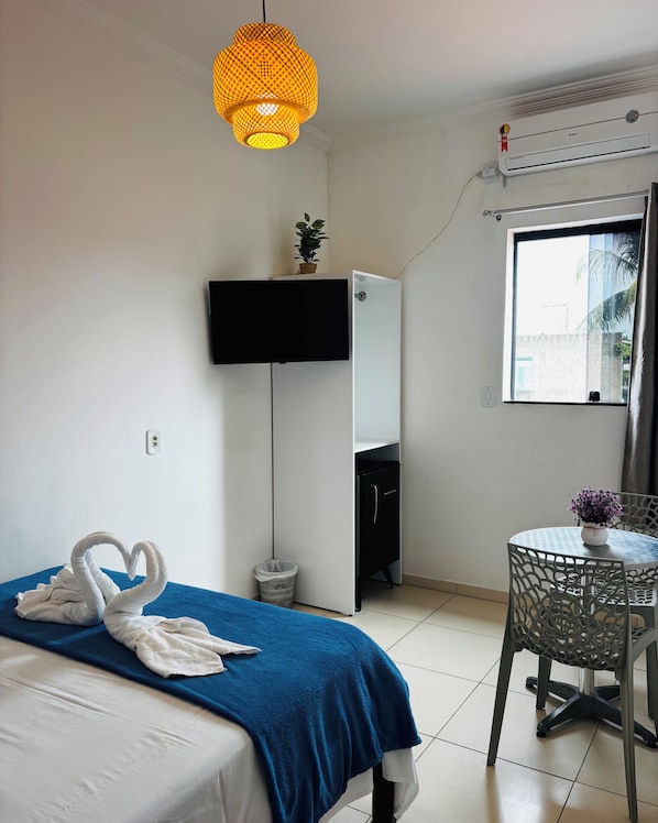 A hotel room with a bed, a desk, a chair, a TV, a potted plant, and a window.