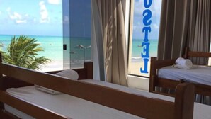 A hotel room with a view of the beach and ocean. There are two wooden beds with white linens. - Maraga Beach Hostel (Maragogi)