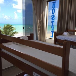A hotel room with a view of the beach and ocean. There are two wooden beds with white linens. - Maraga Beach Hostel (Maragogi)