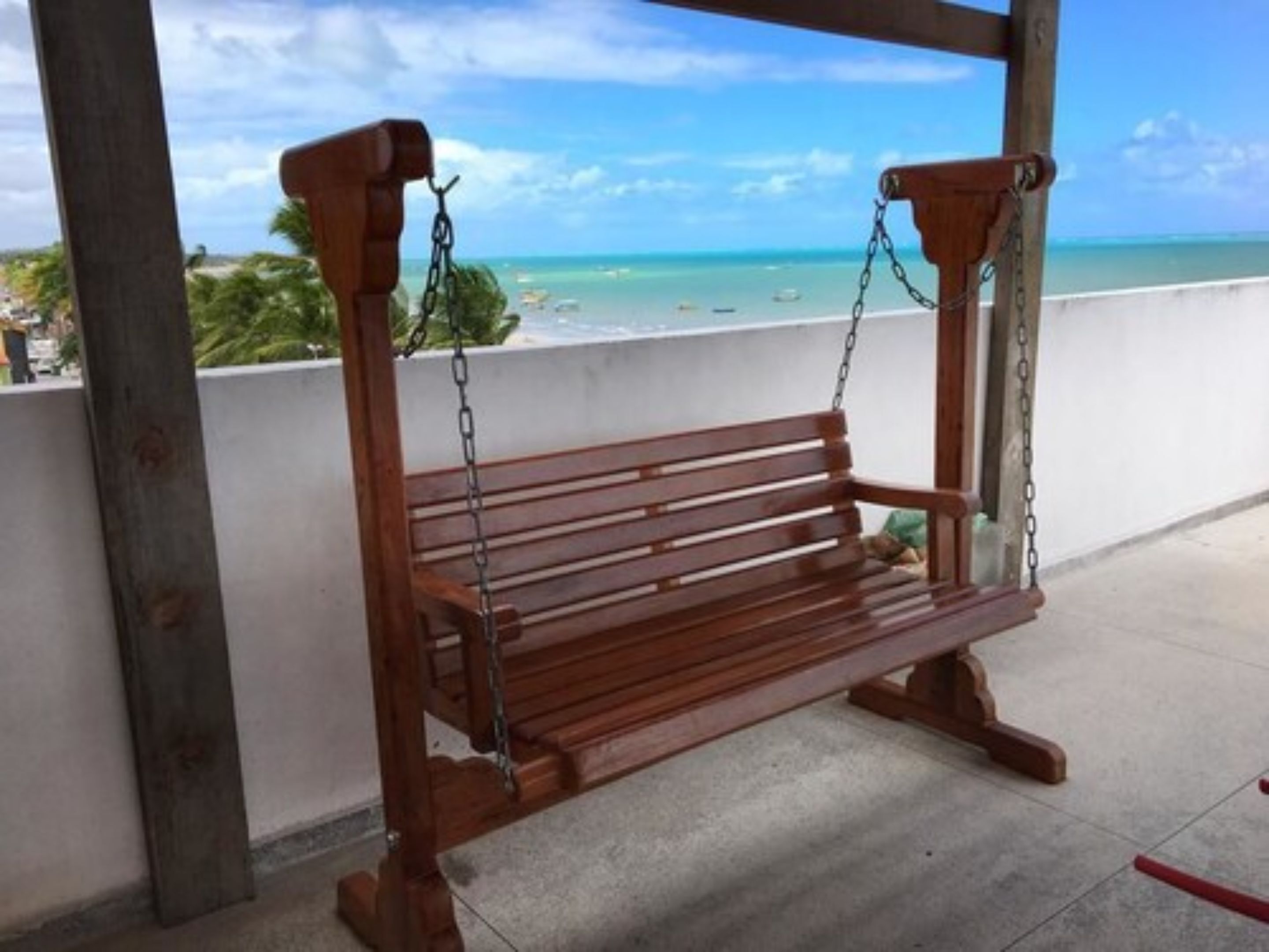 Un banco de madera con cadenas, ubicado en un balcón con vistas a la playa.