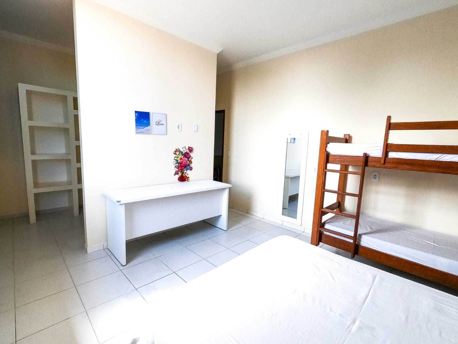 A room with a bunk bed, a white desk, a mirror, and a shelf.