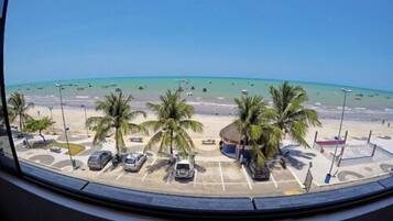A beach view from a window with parked cars and palm trees.