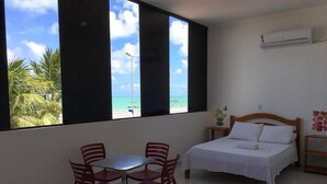 A room with a bed, a table with chairs, and a view of the beach. - Maraga Beach Hostel (Maragogi)