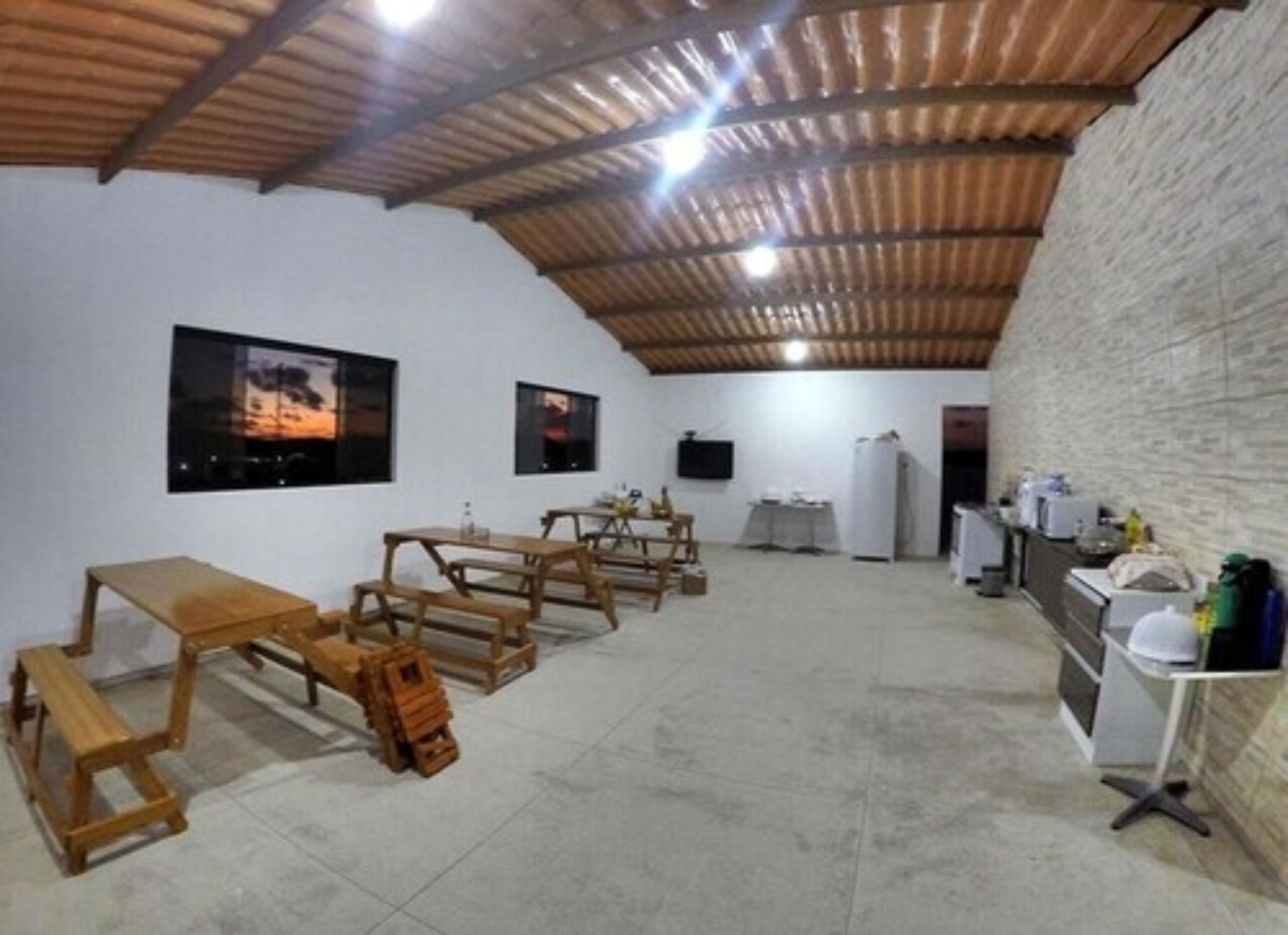 Una habitación espaciosa con techo alto, bancos de madera, una mesa y un refrigerador.