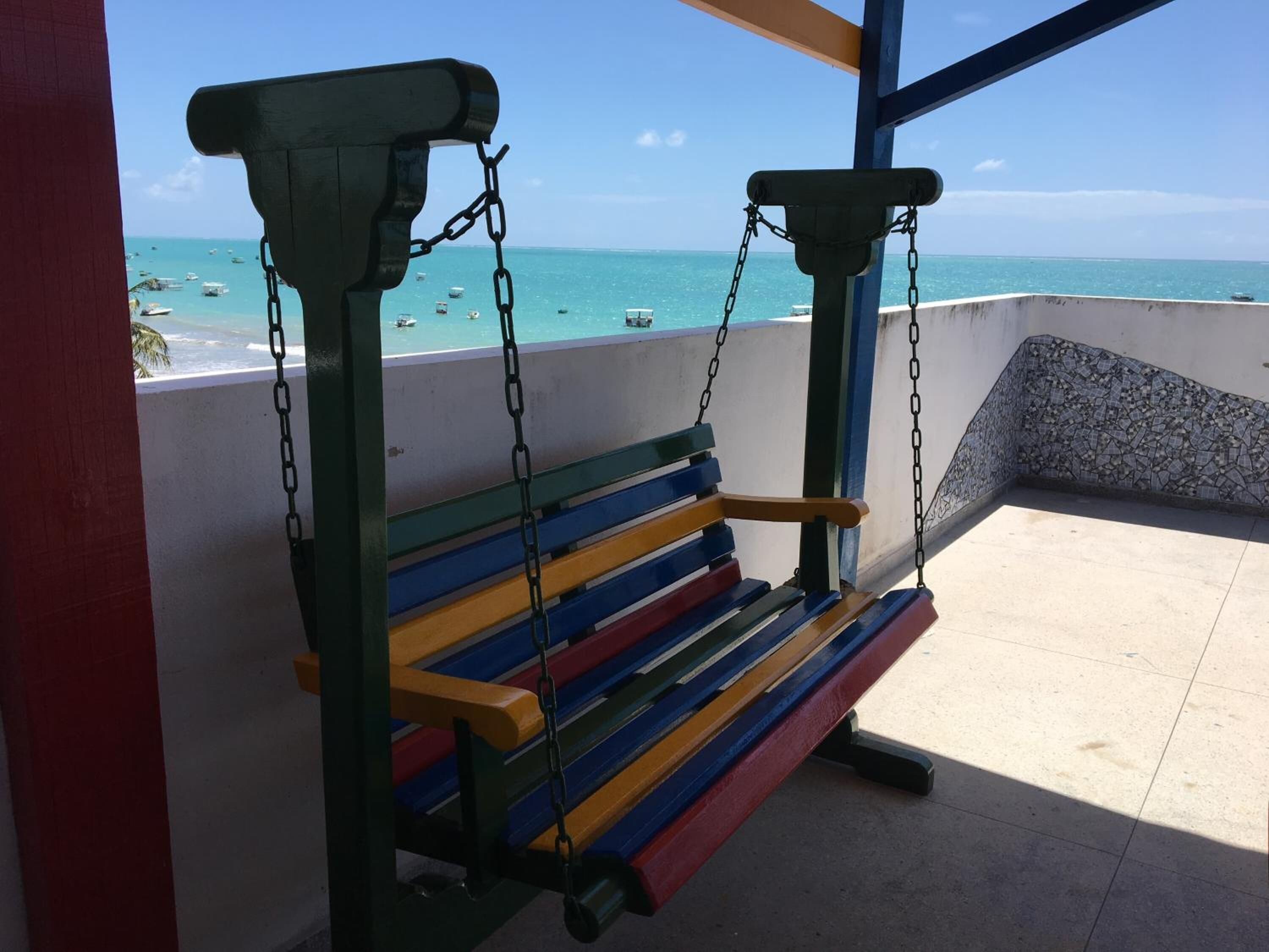 A colorful swing bench overlooking a beach with boats in the water.
