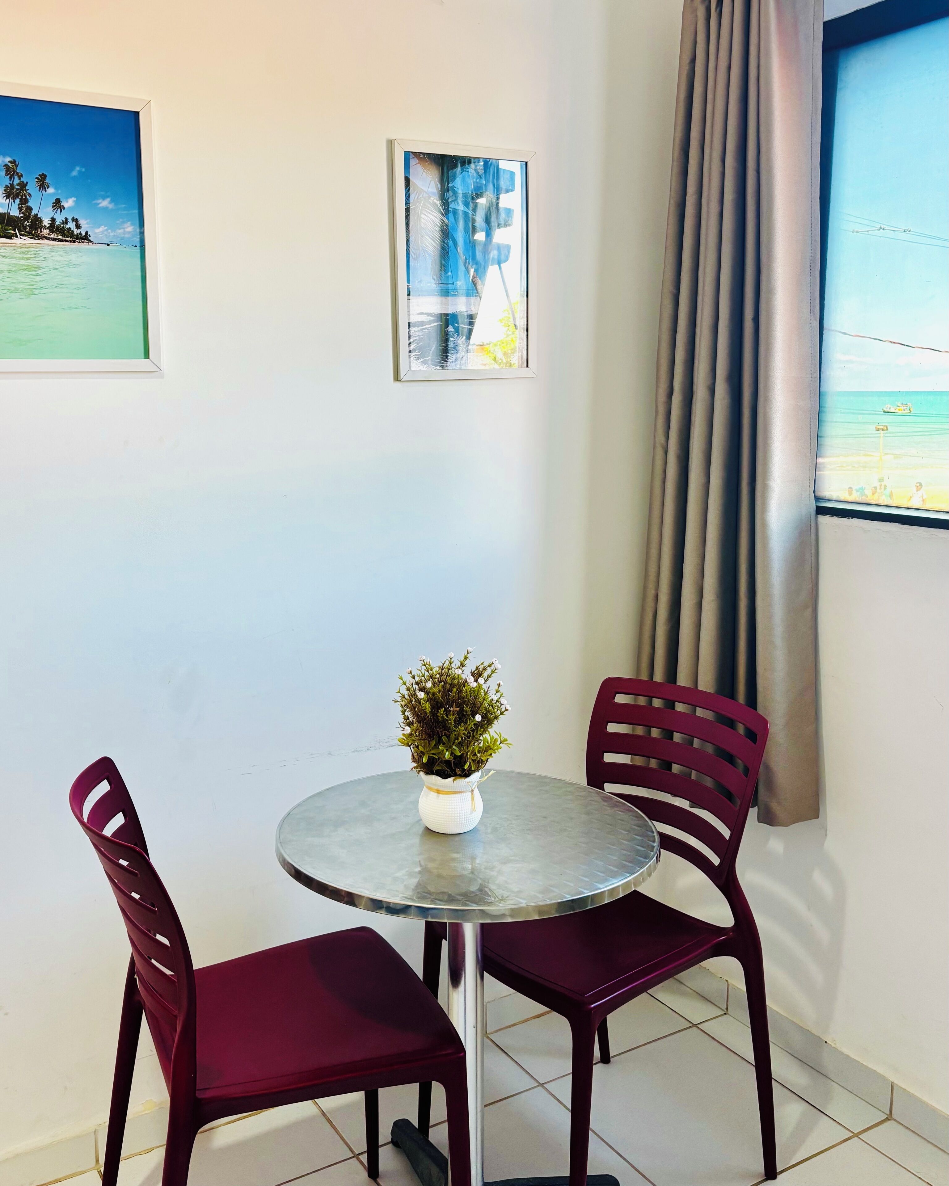 A room with a round table, two chairs, a potted plant, and two framed pictures on the wall.