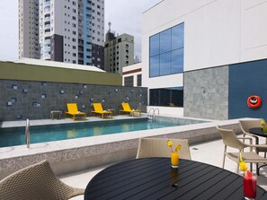 A rooftop pool area with lounge chairs, a table with drinks, and a lifebuoy on the wall.