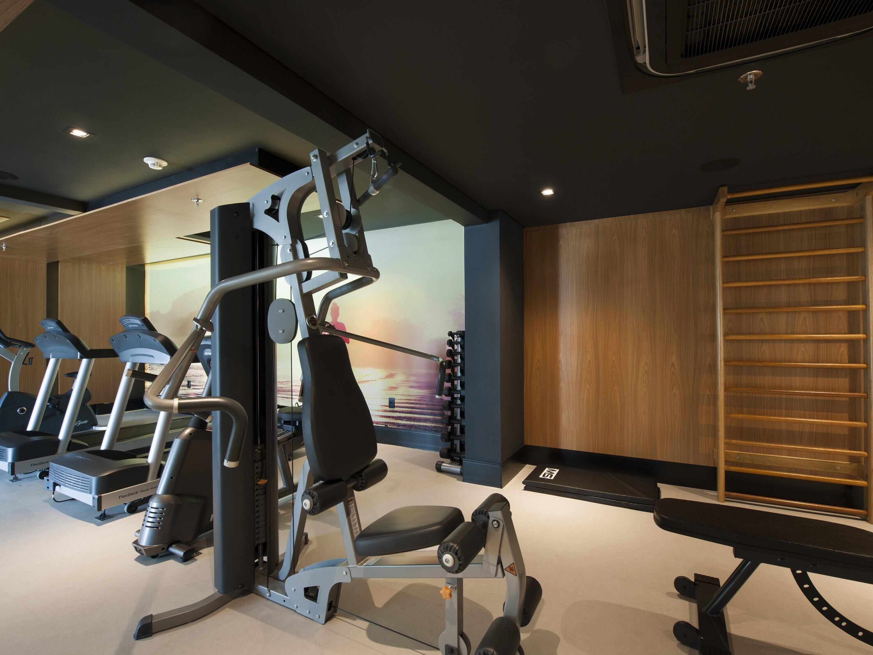 A gym with treadmills, weight machines, and a wooden wall.