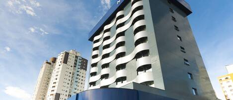 Edificio de un hotel Novotel con diseño moderno, múltiples balcones y un cielo despejado al fondo.