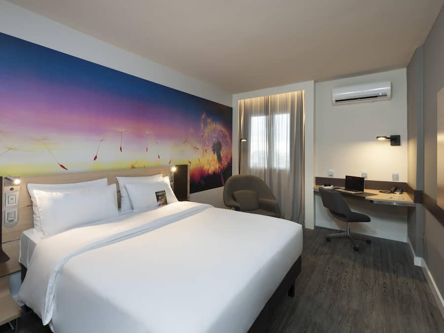 A hotel room with a bed, a desk, an air conditioning unit, and a large wall mural.