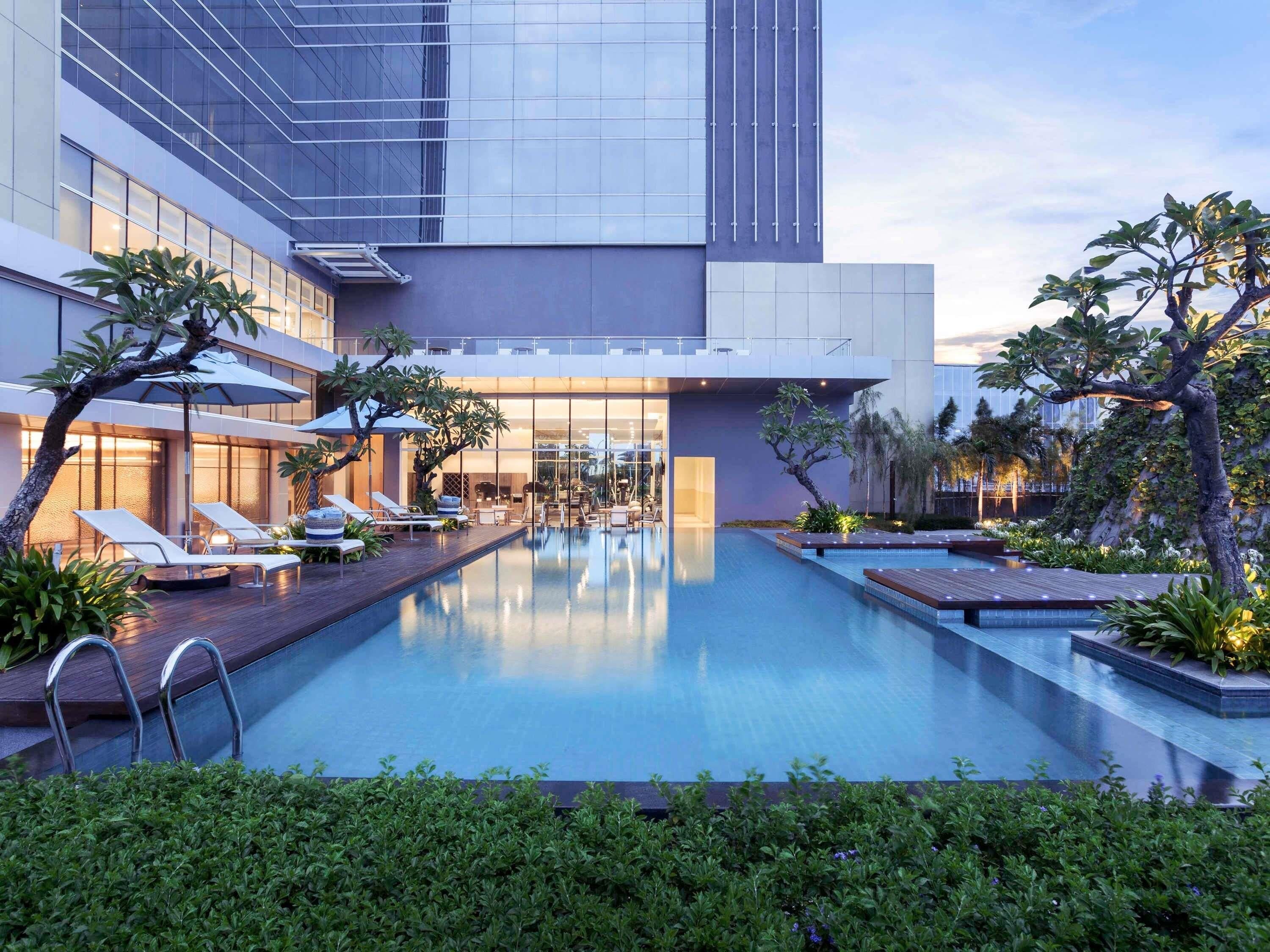 Un hotel moderno con piscina, sillas de descanso y un jardín bien cuidado.