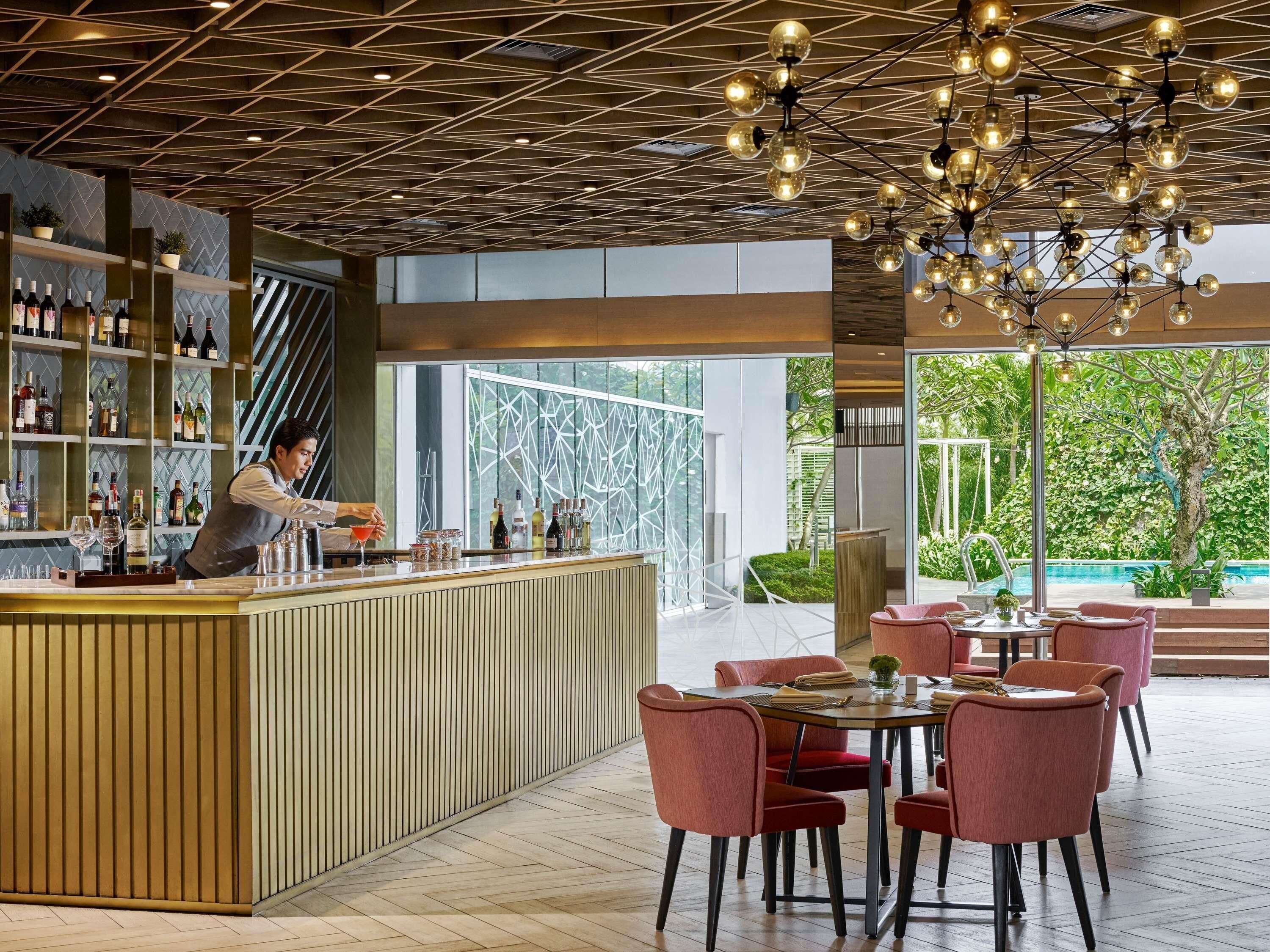 A modern bar area with a bartender, a wooden counter, and a seating area with red chairs.