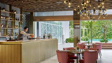 A modern bar area with a bartender, a wooden counter, and a seating area with red chairs.