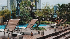 Un espace aménagé au bord de la piscine, avec des chaises longues et des parasols, une terrasse en bois et un bâtiment moderne en arrière-plan.