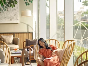A room with a sofa, chairs, a lamp, and a view of greenery outside. - Mercure Jakarta Pantai Indah Kapuk (Jakarta)