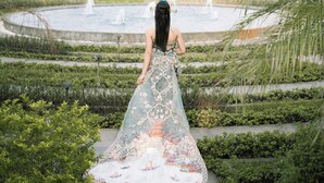 Una mujer con un vestido largo parada en un jardín con una fuente.