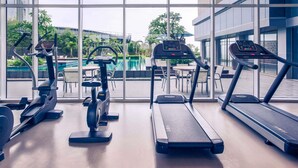 Une salle de sport équipée de tapis de course, d’un vélo elliptique et d’un rameur, avec vue sur une piscine et des palmiers.