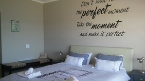 Una cama bien hecha con toallas enrolladas, una cita motivacional en la pared y una mesita de noche con lámpara.