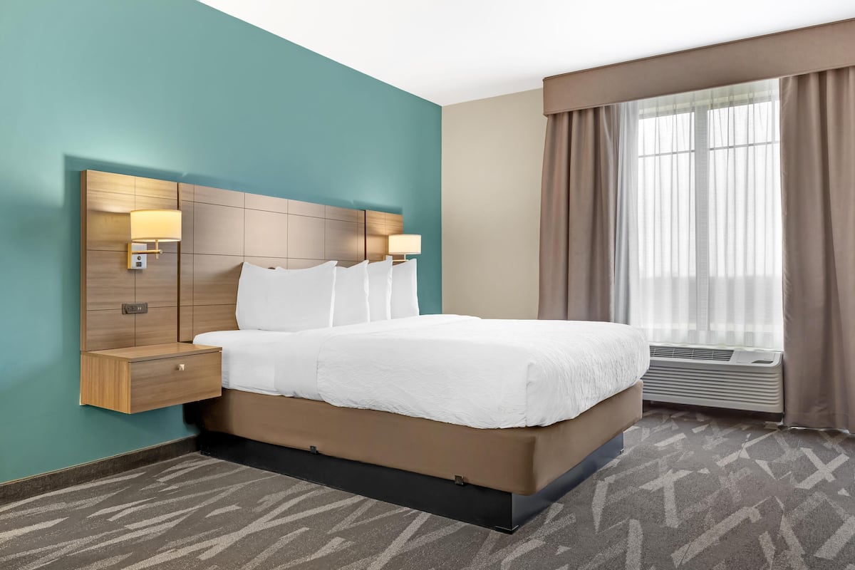 A hotel room with a bed, bedside tables, a wall-mounted lamp, and a large window with curtains.
