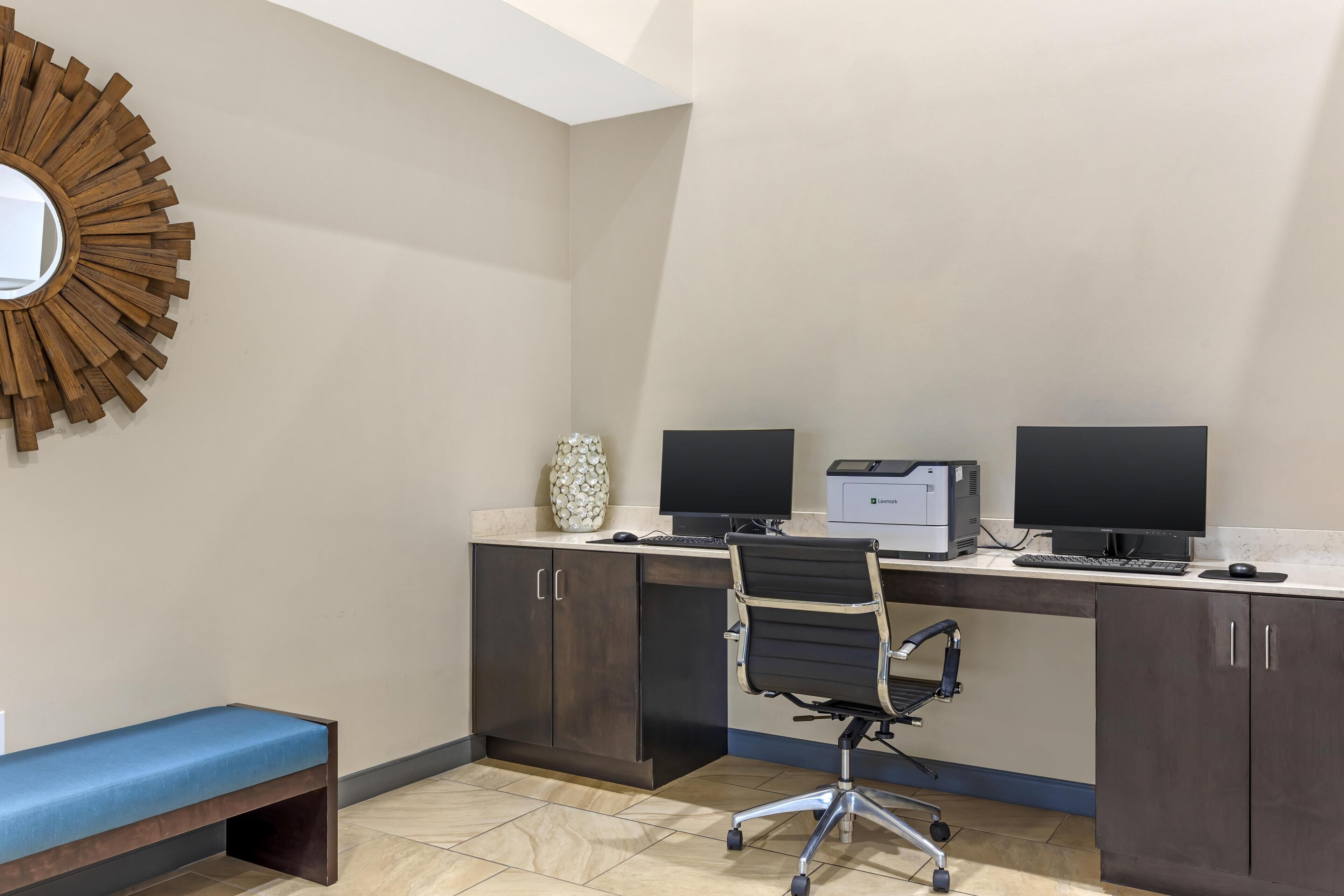A modern office space with a desk, two monitors, a chair, and a bench.